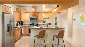 A modern kitchen with wooden cabinets, stainless steel appliances, and a central island with bar stools. - Terracotta Cove - Hot tub, Fire pit, Stargazing (Cornville)