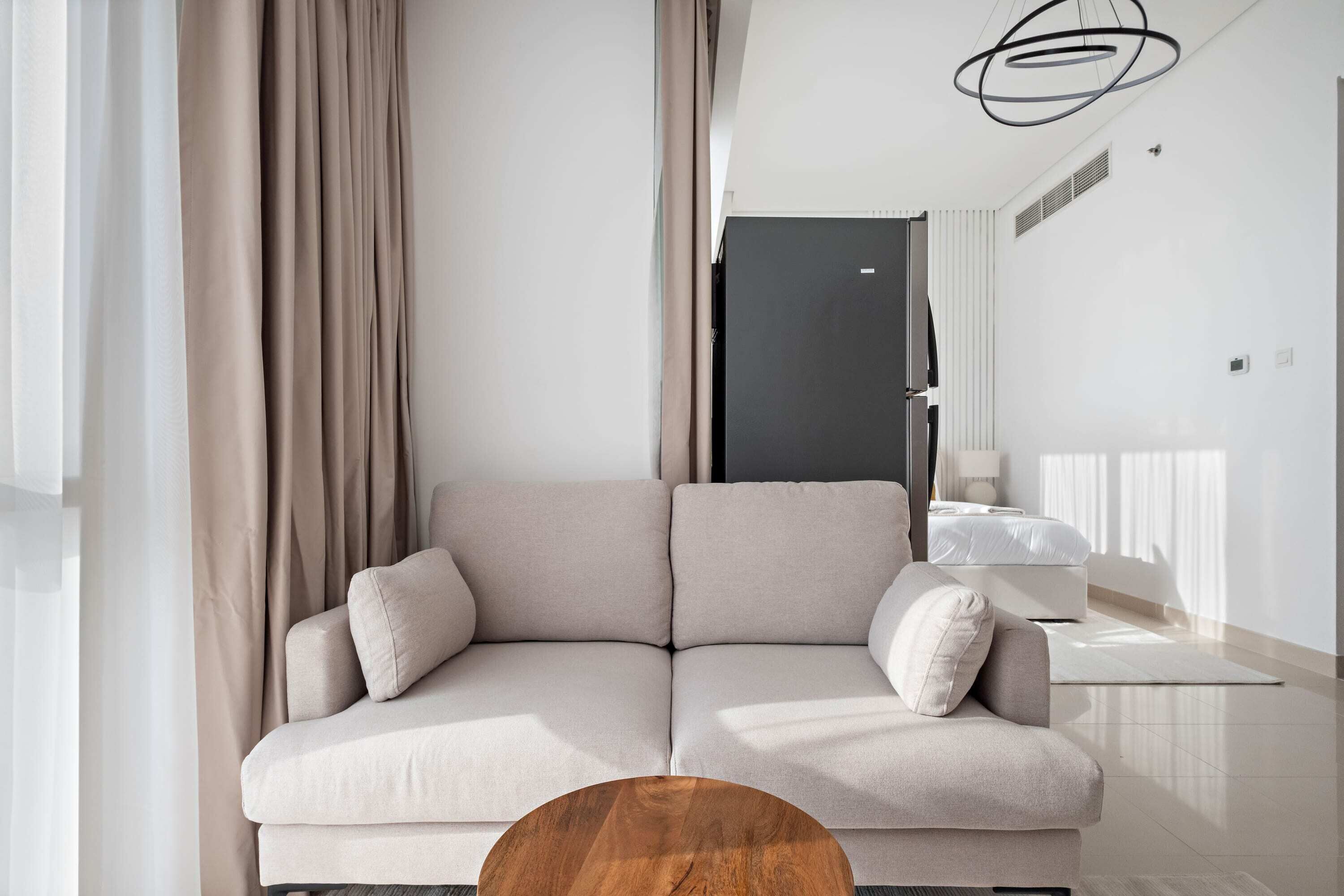 A modern living room with a beige sofa, a wooden coffee table, and a black ceiling light fixture.