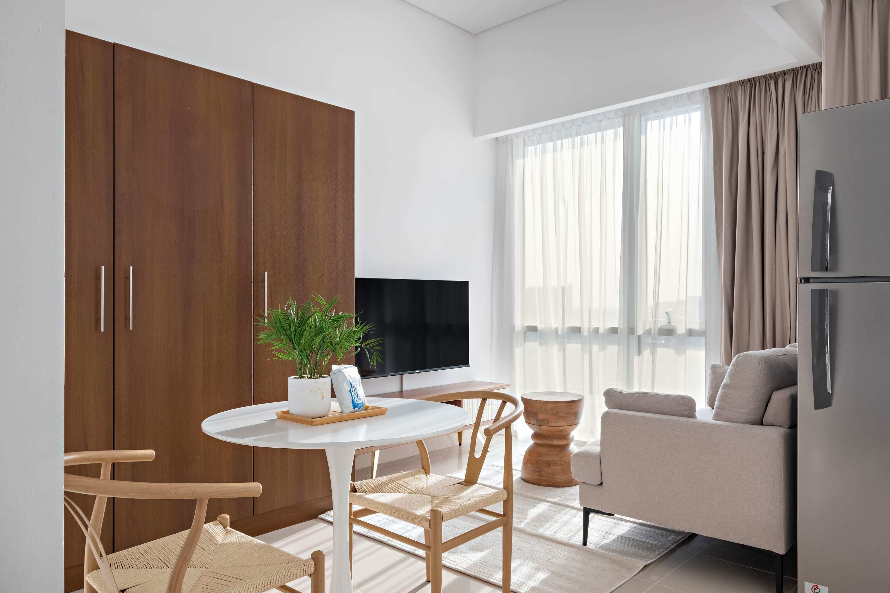 A modern living room with a sofa, a dining table with chairs, a TV, and a large wooden wardrobe.