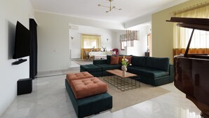 Un salon moderne avec un canapé d’angle, un pouf et un téléviseur à écran plat.