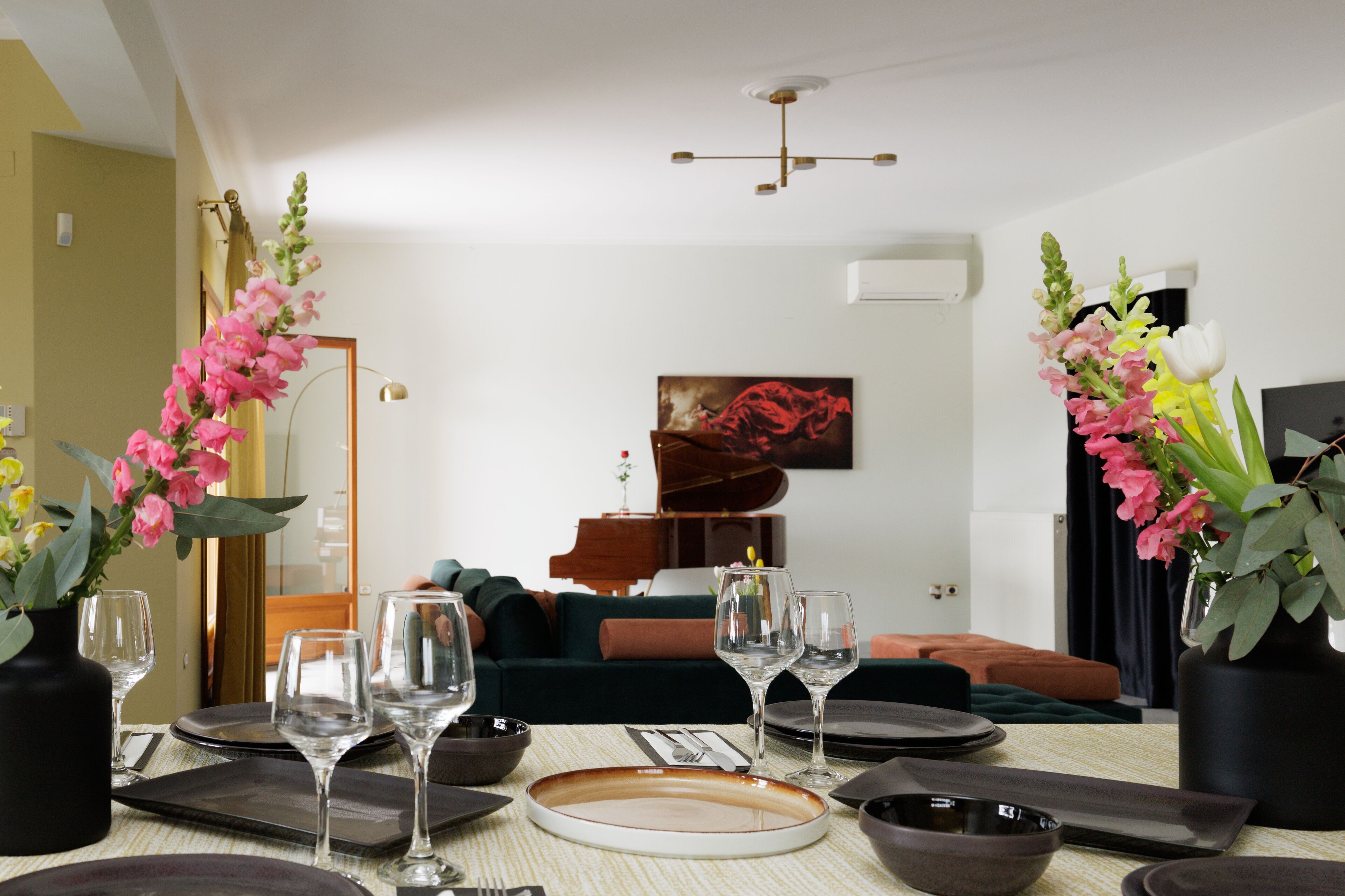 A dining area with a table set for four, a piano in the background, and a sofa.