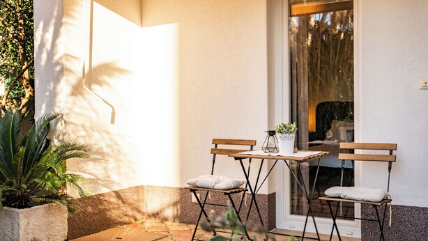 A patio with two wooden chairs and a table, a potted plant, and a window with a view of trees. - Room-apartments & Rooms Buble - Studio w (Trogir)