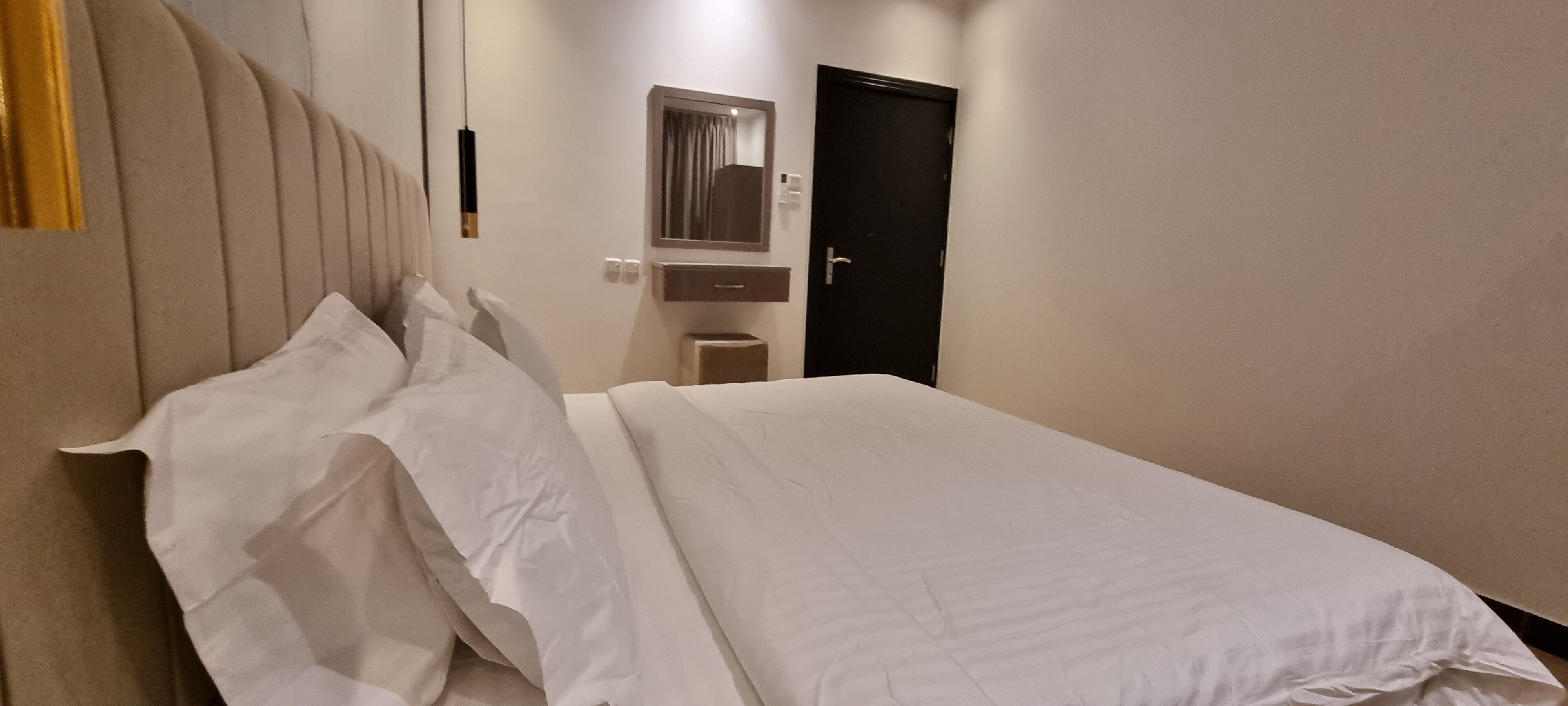 Een hotelkamer met een bed, nachtkastje, spiegel en deur.