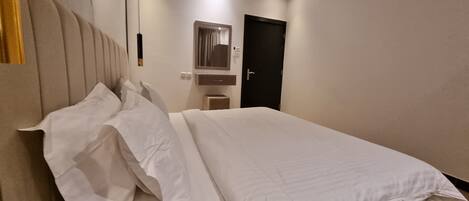 Een hotelkamer met een bed, nachtkastje, spiegel en deur.