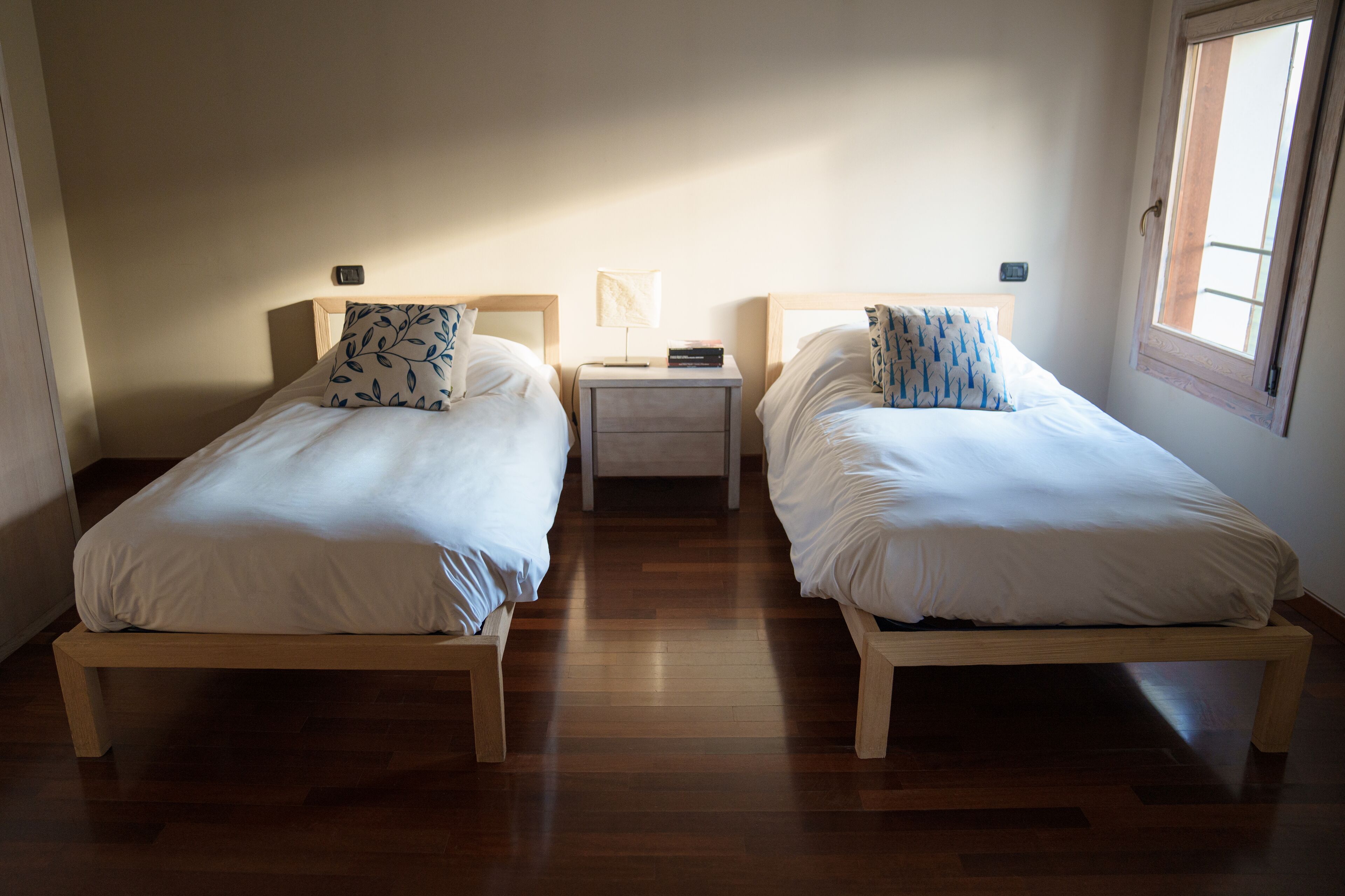 Une chambre avec deux lits, un plancher en bois et une table de chevet placée entre les deux.
