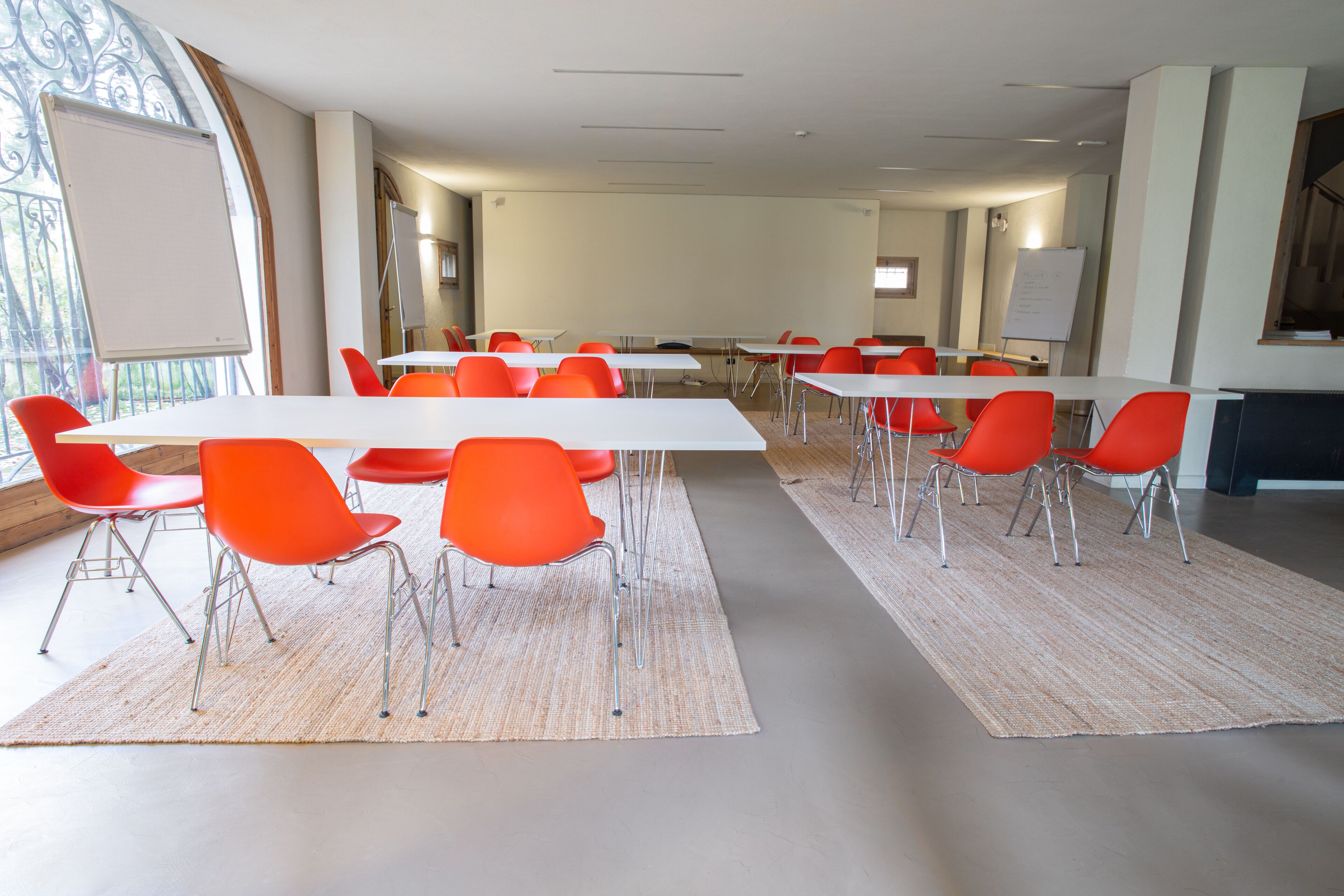 Une salle de conférence avec des tables blanches et des chaises orange, de grandes fenêtres et un tableau blanc.