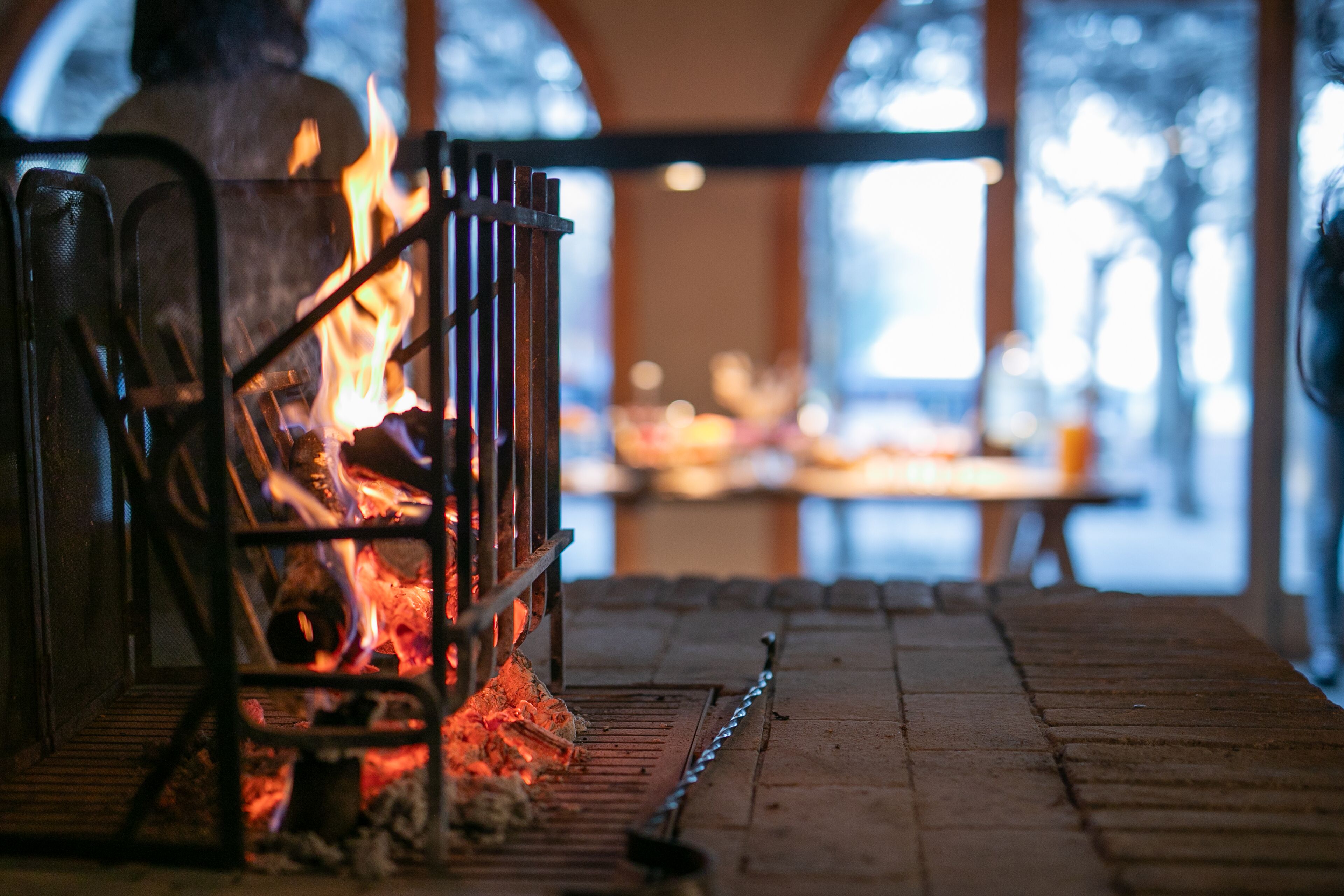A fireplace with visible flames, a metal grate, and a brick floor.