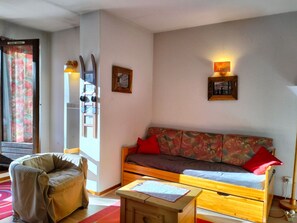 A cozy living room with a sofa, a chair, and a small table. There are two wall-mounted lights and a framed picture above the sofa.
