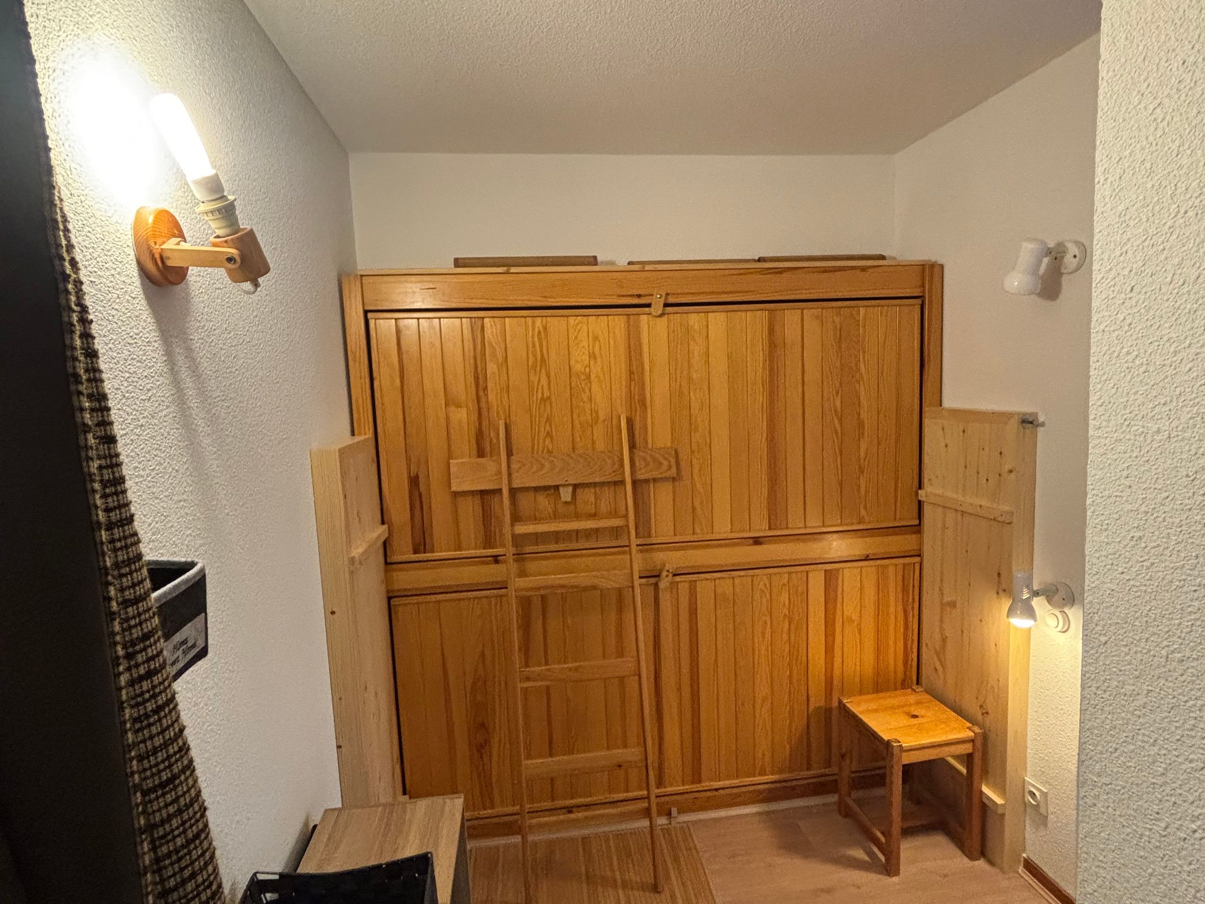 Una stanza con un'armadiatura in legno, un piccolo sgabello di legno e un faretto a parete.
