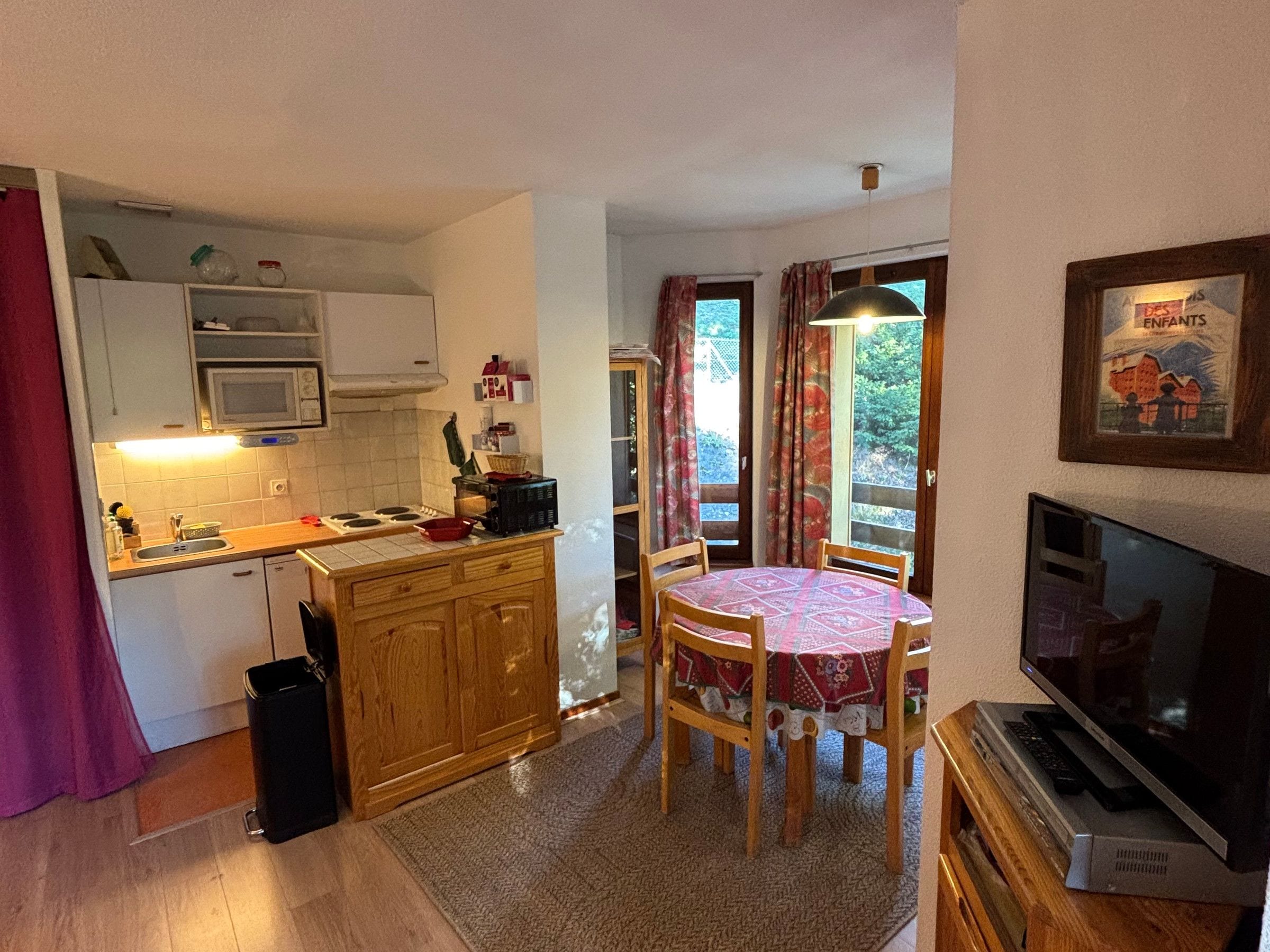 A compact kitchen with a microwave, stove, and sink, a dining area with a table and chairs, and a television on a wooden stand.