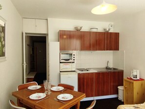 A compact kitchen with wooden cabinets, a built-in oven, a sink, and a dining area with a table set for four.
