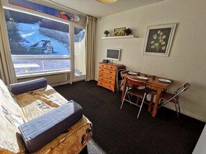 A room with a bed, a desk with a computer, a chair, and a window with a view of a snowy landscape.