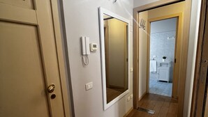 En hall med en dörr av trä, en väggmonterad lampa, en övervakningskamera och en spegel.
