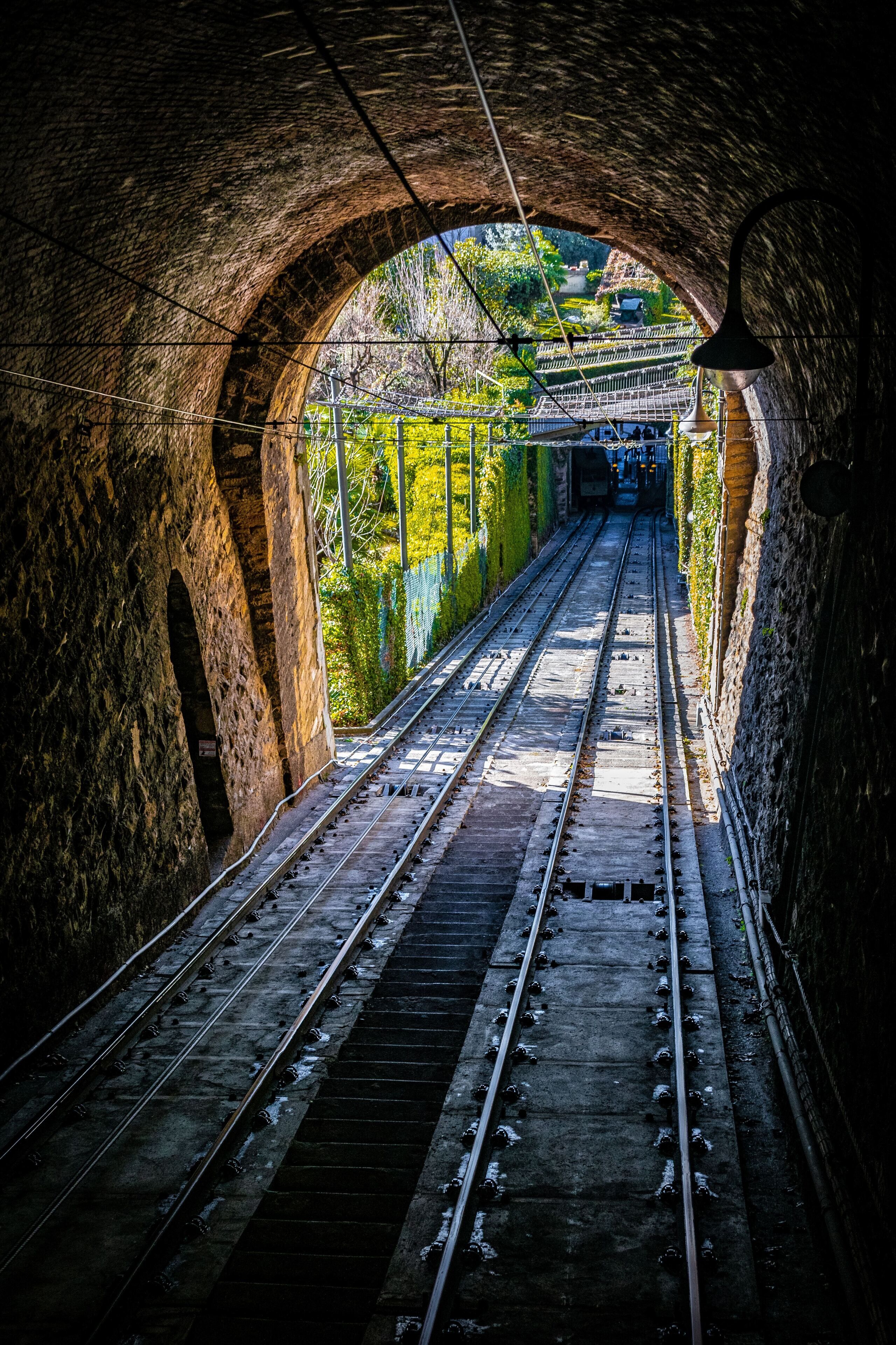 Ein Bahntunnel mit Gleisen, Steinwänden und einem Metallpfosten.