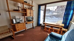 Une pièce chaleureuse avec un bureau en bois, un canapé bleu et une grande fenêtre donnant sur un paysage enneigé.