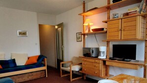 Un espace de vie compact comprenant un canapé, une table à manger avec assiettes et verres, un téléviseur et une machine à café.