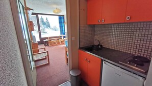 Une cuisine compacte avec des meubles de couleur orange, un dosseret carrelé et une vue sur l’espace repas à travers une porte ouverte.