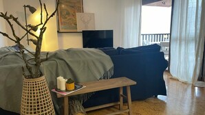 Ett mysigt vardagsrum med en soffa, ett litet träbord, en dekorativ gren i en flätad korg och en inramad tavla på väggen.