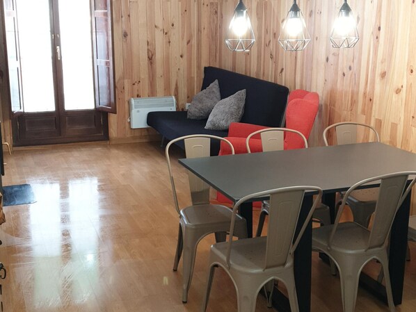 Una habitación con pared de madera, un sofá con cojines rojos y grises, una mesa con sillas y un calentador.