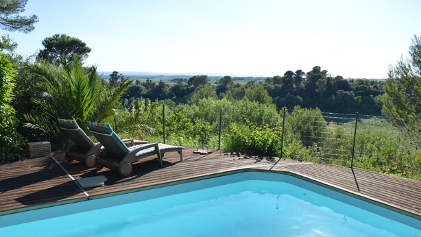 A swimming pool with lounge chairs and a wooden deck, surrounded by greenery and a view of the countryside.