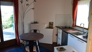 A compact kitchen with a dining area, a refrigerator, a sink, and a window with curtains.