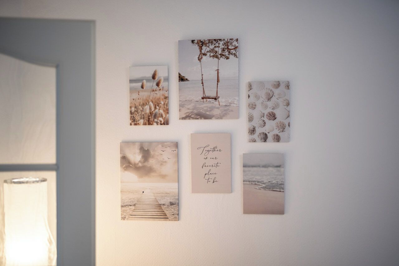 A wall with five framed pictures depicting beach scenes, including a swing, a pier, and a seashore.