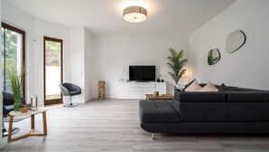 Una sala de estar moderna con un sofá gris, un televisor de pantalla plana, una mesa de centro de madera y una planta en maceta.