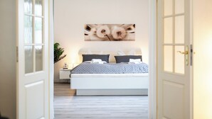 Un dormitorio con cama, mesita de noche, planta en maceta y una obra de arte colgada en la pared.