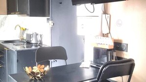 Eine kompakte Küche mit Essbereich, einem an der Wand befestigten schwarzen Fernseher und einem Fenster, das für natürliches Licht sorgt.