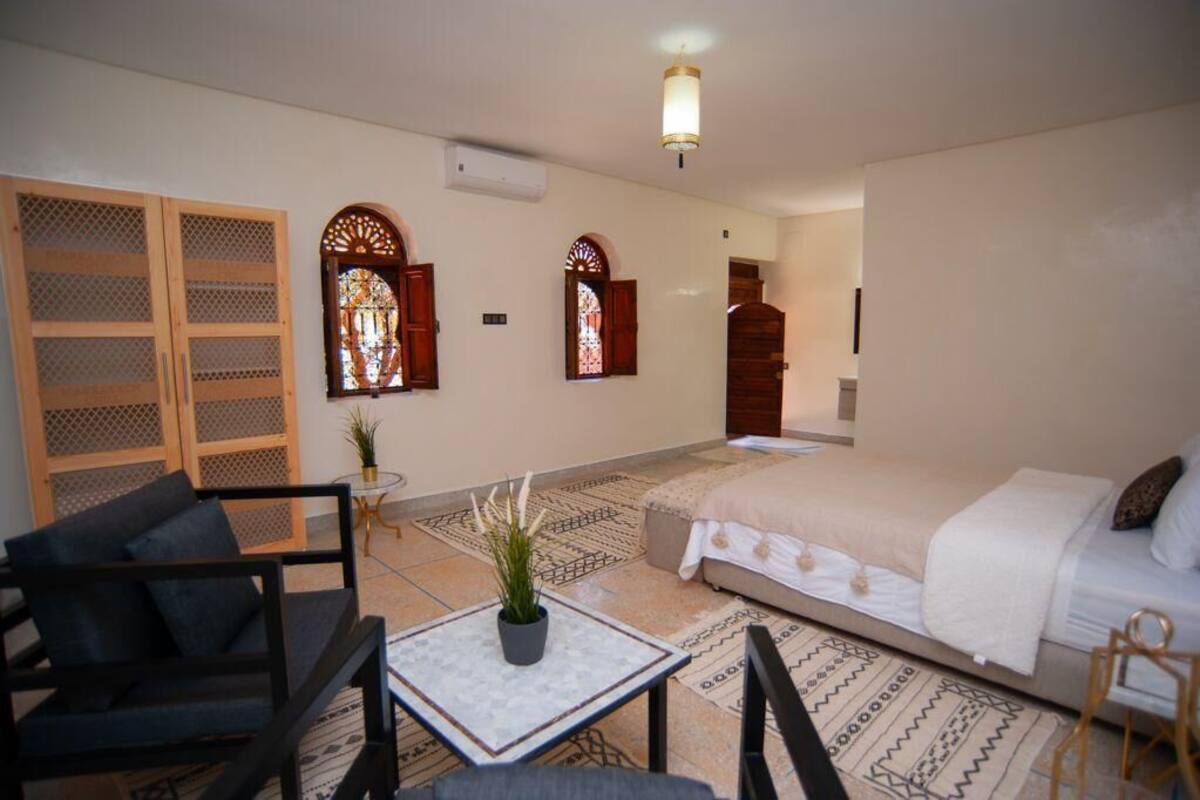 A bedroom with a bed, a small table with a plant, a sofa, and two chairs.