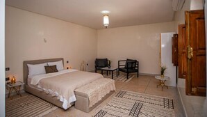 Un dormitorio con cama, escritorio, dos sillas, una mesita y un aire acondicionado de pared.