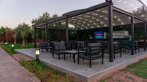 Un patio al aire libre con asientos y una pantalla de televisión, rodeado de vegetación.