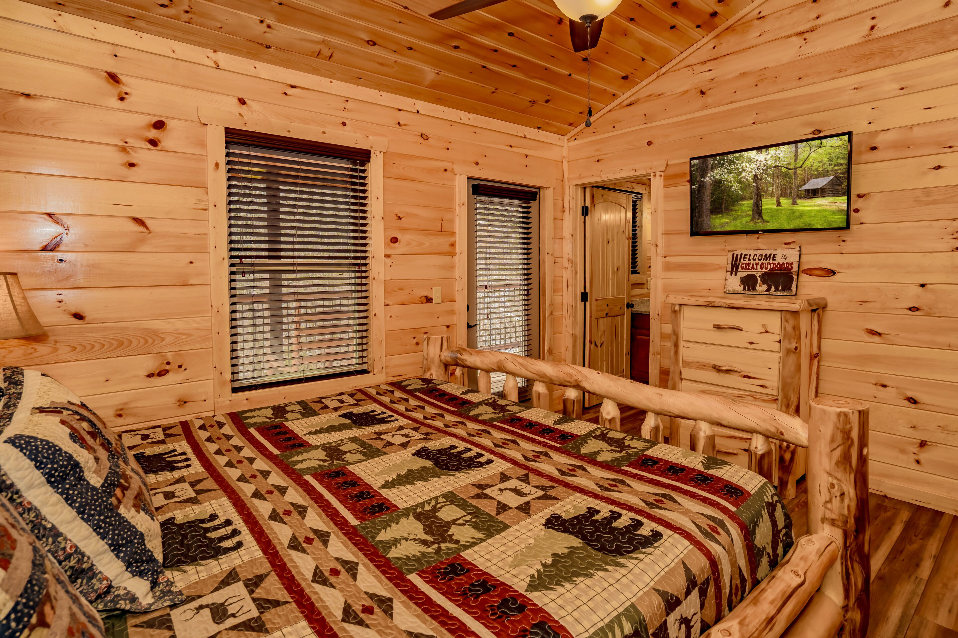 Quarto de cabana de toras com uma cama, uma televisão e um letreiro dando as boas-vindas aos hóspedes para a natureza.