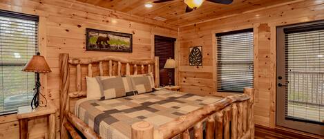 A wooden cabin bedroom with a bed, ceiling fan, and wooden walls.