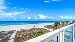Blick auf den Strand vom Balkon aus, mit blauem Himmel, Sandstrand und Palmen.