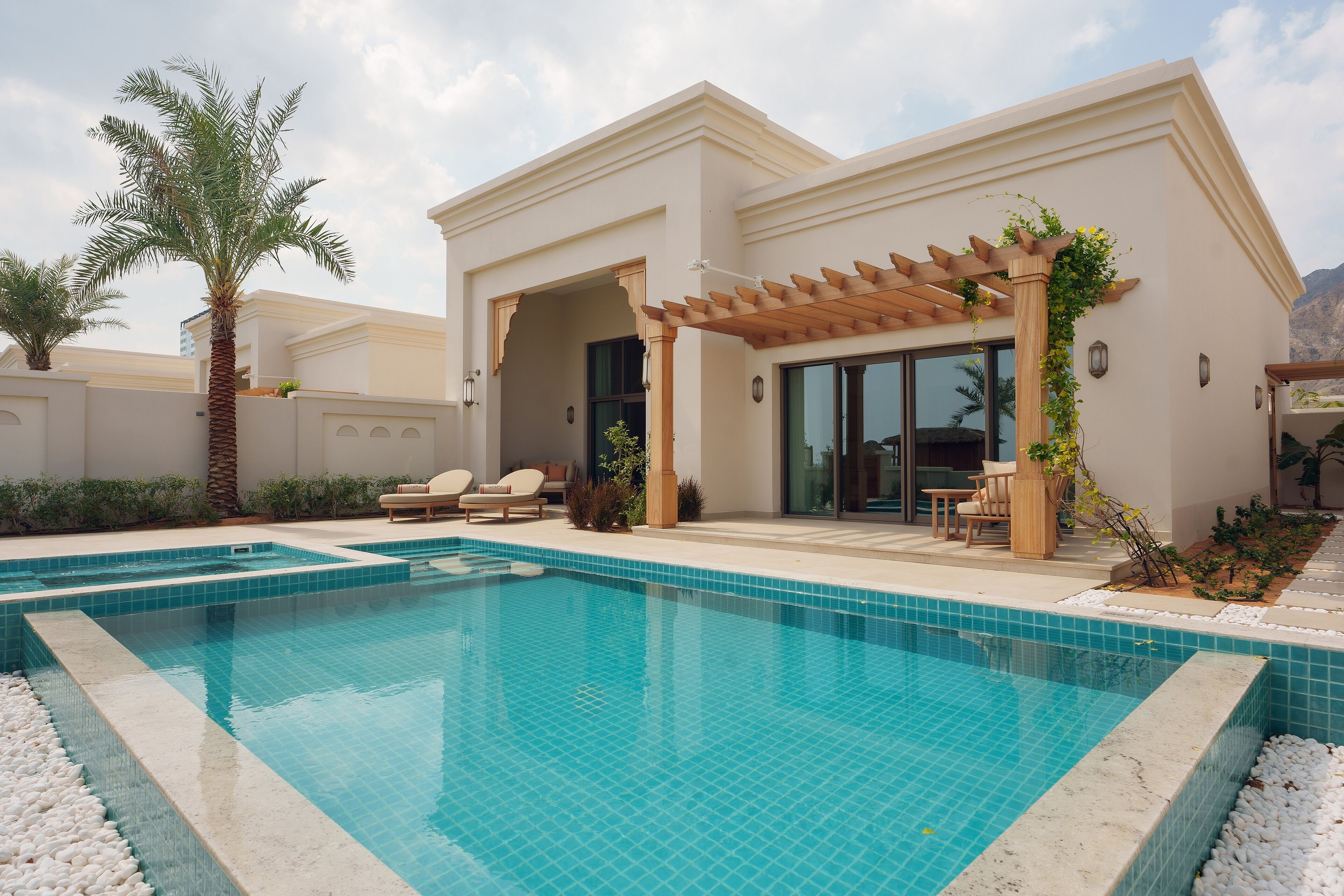 Ein moderner Poolbereich mit einem klaren, blauen Pool, einer weißen Fliesenveranda und einem Pergola, das mit Kletterpflanzen bewachsen ist.