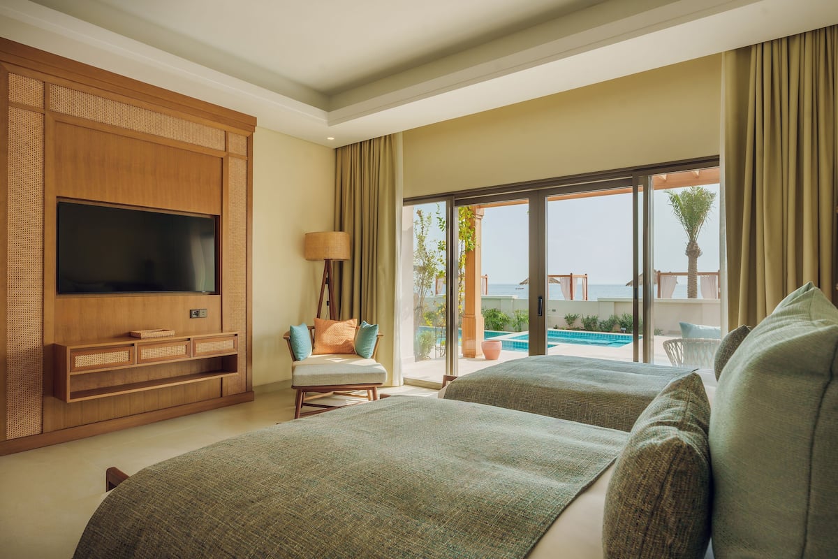 Ein Hotelzimmer mit großem Fernseher, einer Couch, einem Sessel und einem Balkon mit Blick auf den Pool.