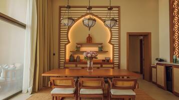 Un comedor con una mesa de madera, cuatro sillas, un jarrón con flores y una pared decorativa con estantes y luces colgantes.
