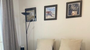 A neatly made bed with folded towels, a standing lamp, and three framed pictures on the wall.