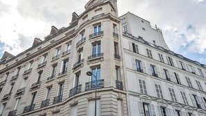 A multi-story building with classical architecture, featuring a prominent corner with a rounded pediment and a balcony.