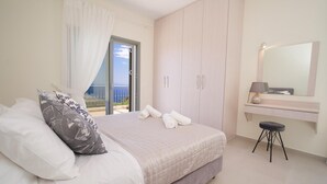 A bedroom with a bed, a nightstand, a mirror, and a view of the sea through a sliding door. - Villa Aglaia in Mavrata (Kefalonia)