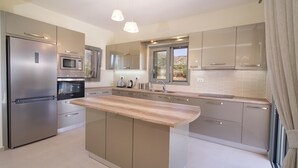 A modern kitchen with stainless steel appliances, a wooden island, and a large window providing natural light. - Villa Aglaia in Mavrata (Kefalonia)