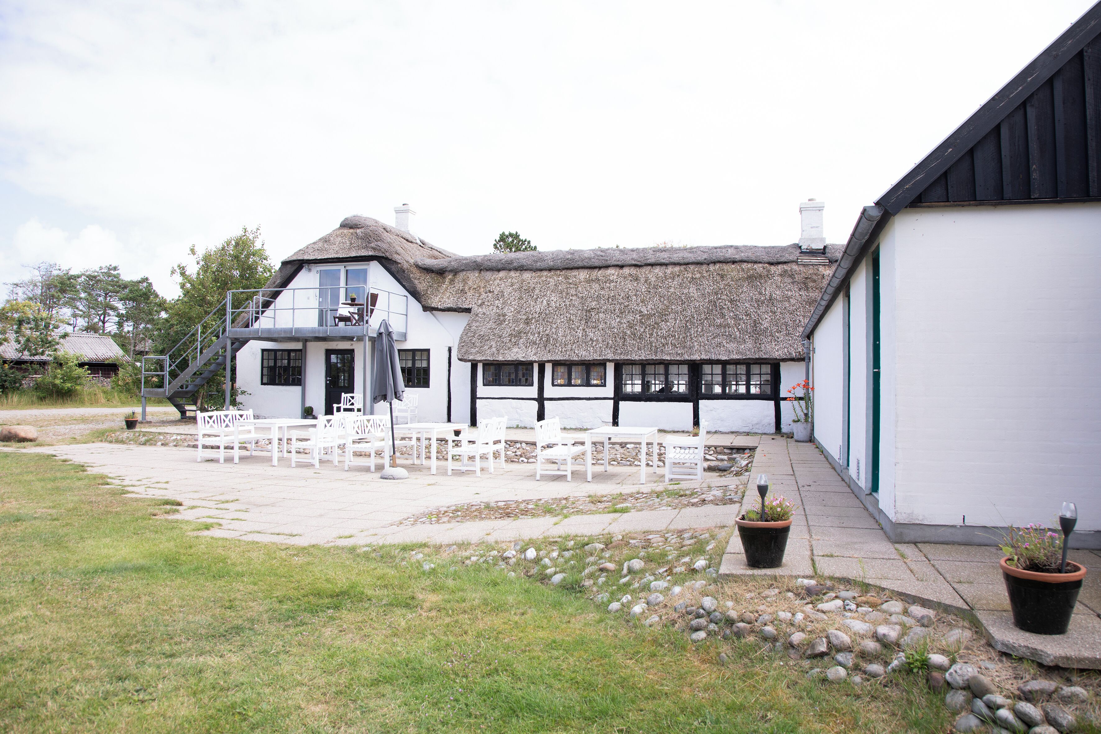 A traditional building with a thatched roof, white walls, and a small outdoor seating area with white furniture.