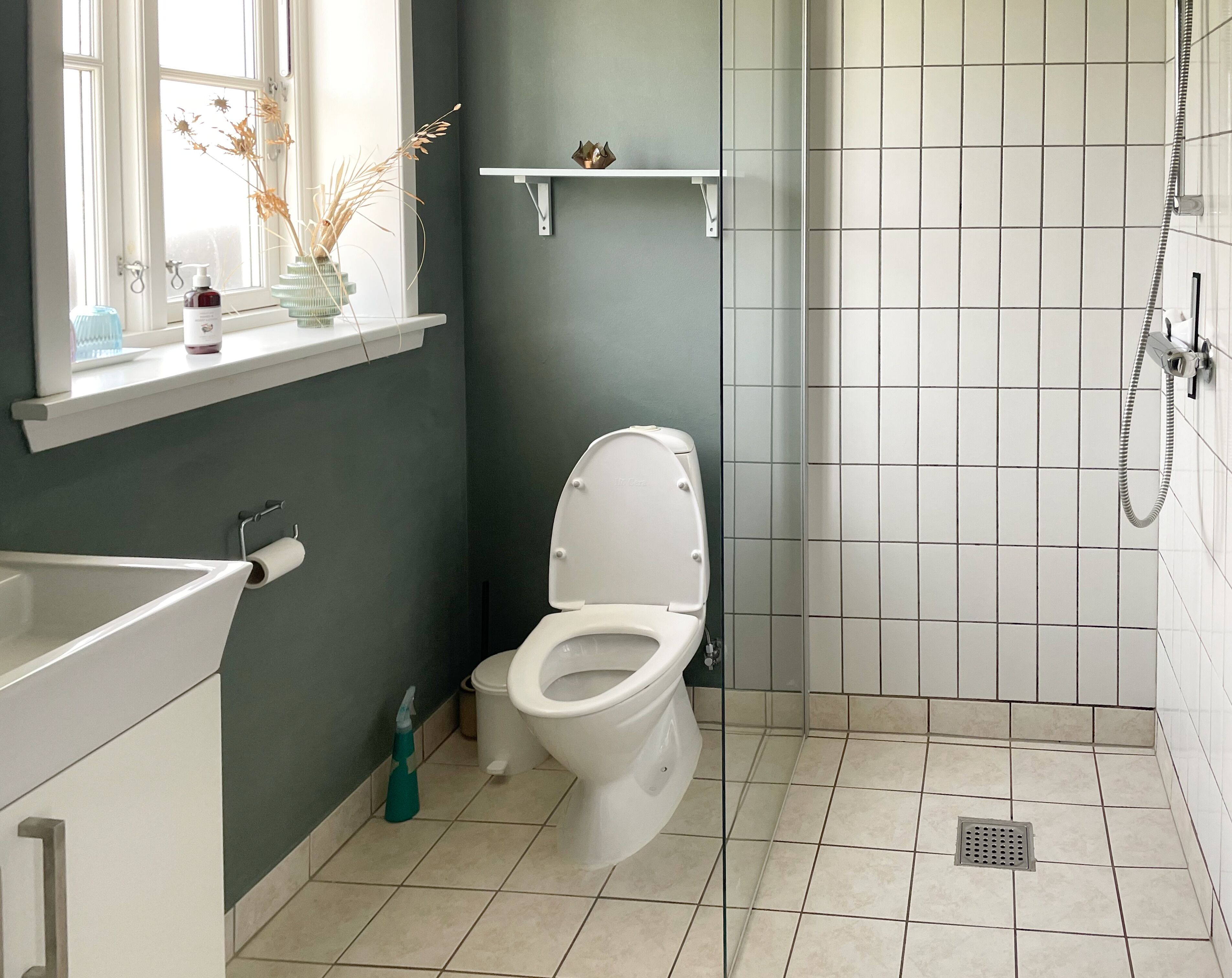 Ein Badezimmer mit Toilette, Dusche und einem Fenster mit einer Vase getrockneter Blumen.