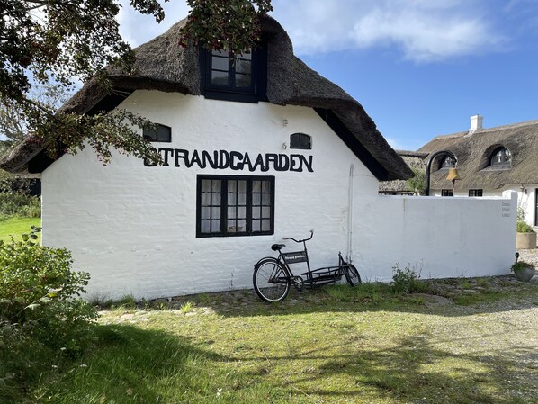 A white building with a black roof, labeled "Strandgarden," and a bicycle parked in front.