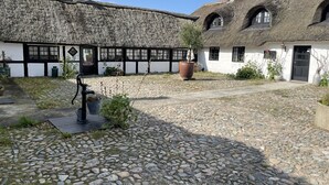 A traditional thatched-roof building with a cobblestone courtyard, a black metal pump, and potted plants. - Hotel Strandgaarden (Læsø)