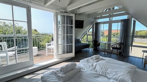 A modern bedroom with a large bed, a sofa, and a balcony with a view. - Hotel Strandgaarden (Læsø)