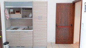 Une cuisine de taille réduite, équipée d’un évier, de placards et d’une porte en bois.