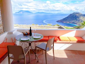Un balcón con una mesa preparada para dos, con vista al mar y una montaña.