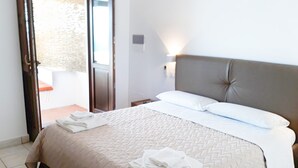 Un lit bien fait, avec une couverture beige et des oreillers blancs, une table de chevet avec une lampe, et une vue sur un espace extérieur grâce à une porte coulissante.